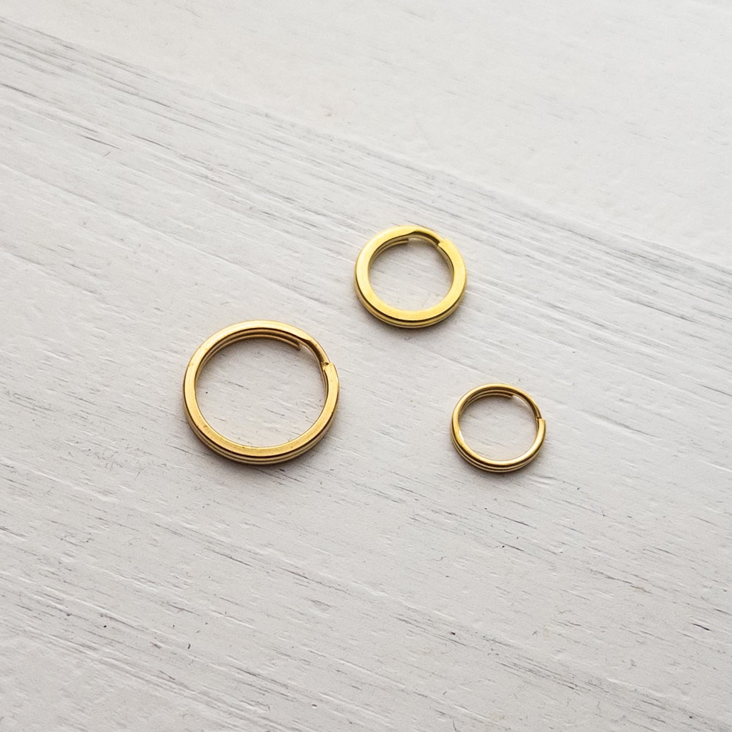 Three solid brass gold split rings on a white textured background. 
