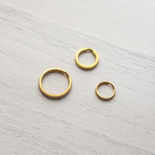 Three solid brass gold split rings on a white textured background. 