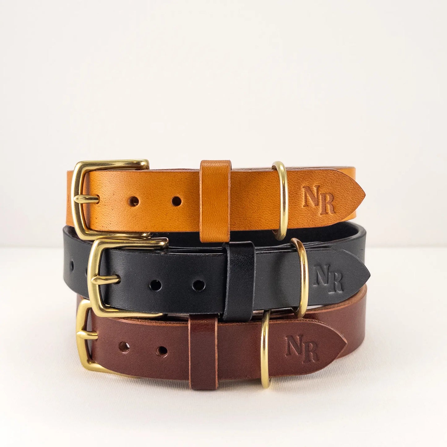 Custom leather dog collars stacked from top: Ochre, Raven, and Walnut, handcrafted with solid brass hardware